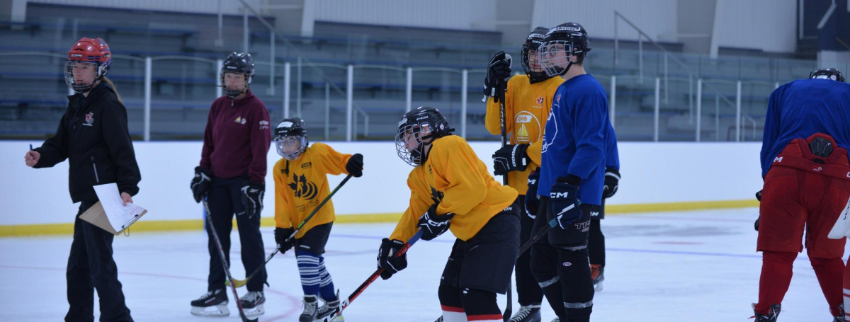 Coach guiding young players on the ice. Players are wearing yellow and blue jerseys