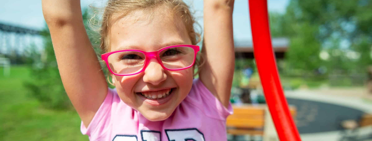 Girl wearing red glasses and pink shirt is smiling and holding her arms over her head.