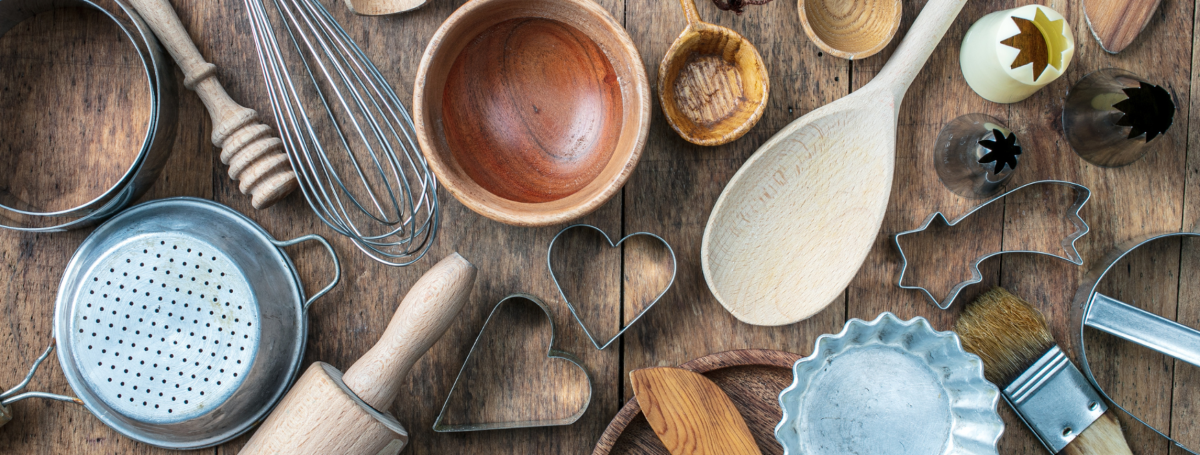Bird's eye view of a variety of baking tools on a wooden table: spoons,, rolling pins, cookie cutters, etc.