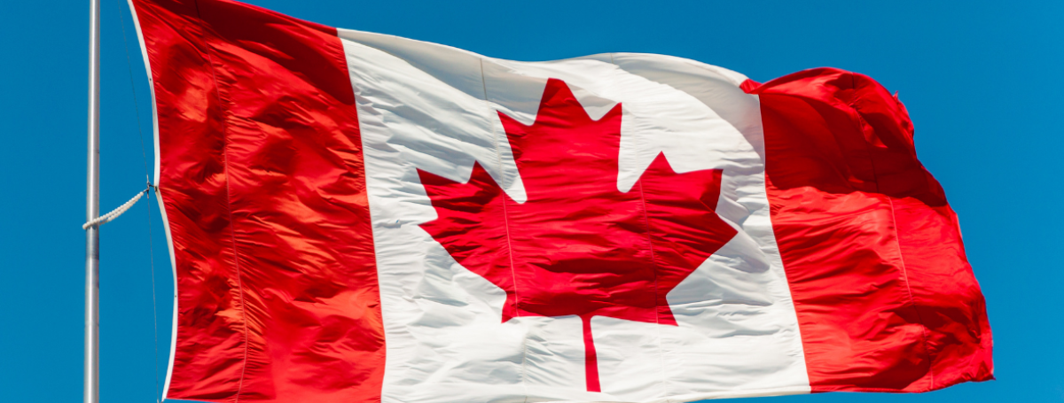 A Canadian flag waves on a flagpole against a bright blue sky.