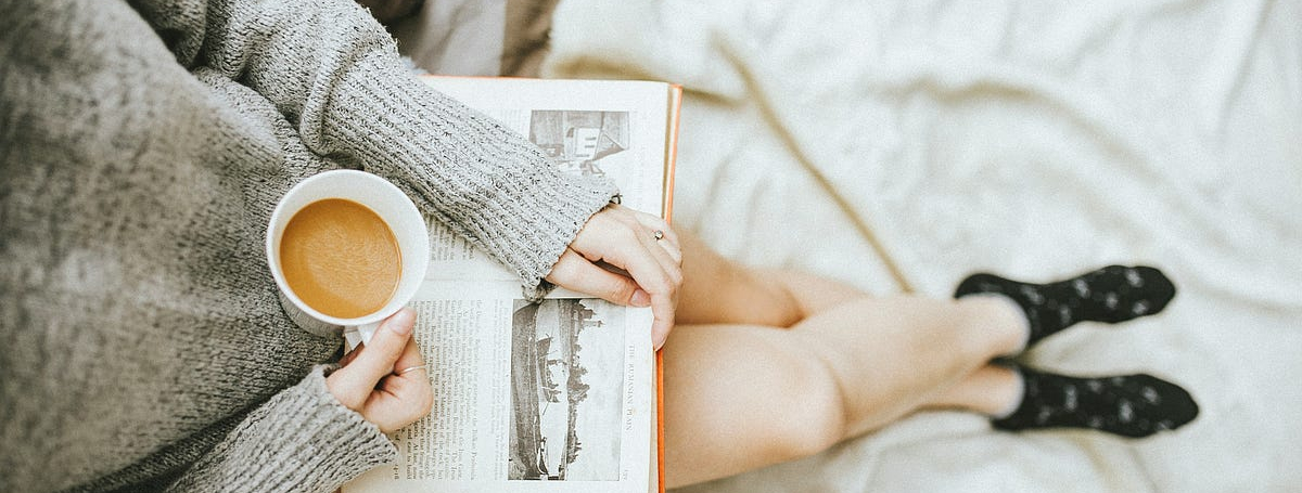 Birds eye view photo of a woman sitting with a coffee and a book on her lap.