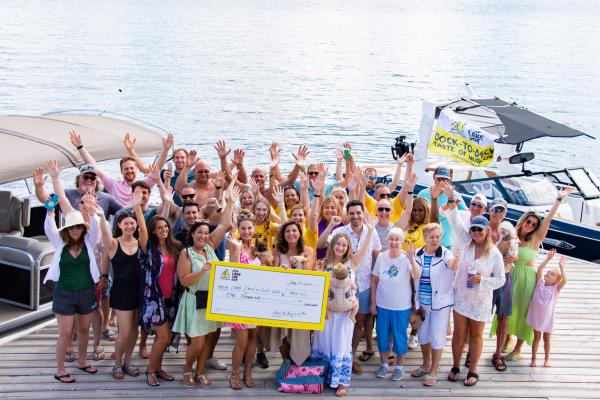 A large group of attendees standing on a doc smiling and waving with a large cheque for CNIB