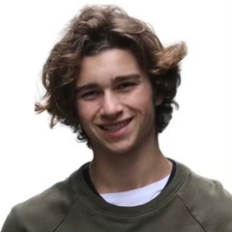 Nico, a young man with brown hair, smiles and poses for a selfie-style photograph. He is wearing a taupe sweater.