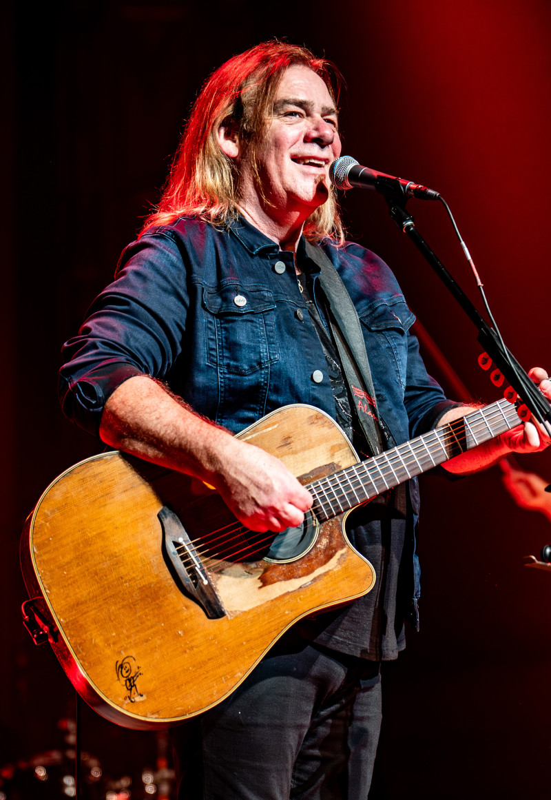 Musician Alan Doyle standing in front of a microphone with a guitar