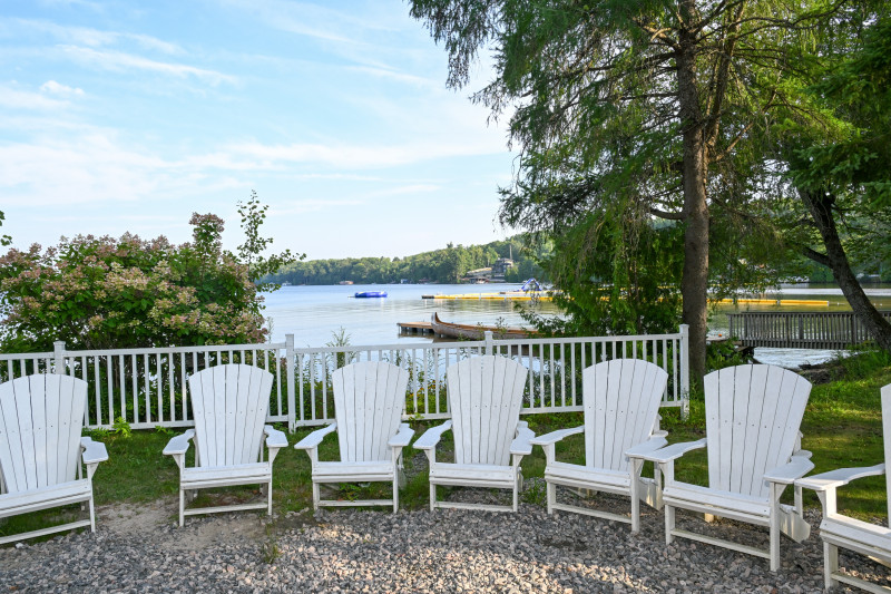 a row of white muskoka chairs in front of the lake 