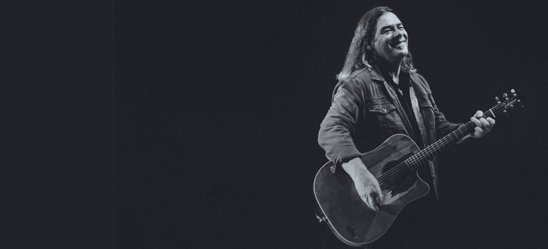 Alan Doyle smiling playing the guitar
