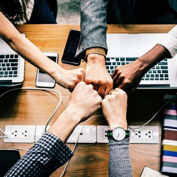 A diverse group of people in a circle fist bump one another