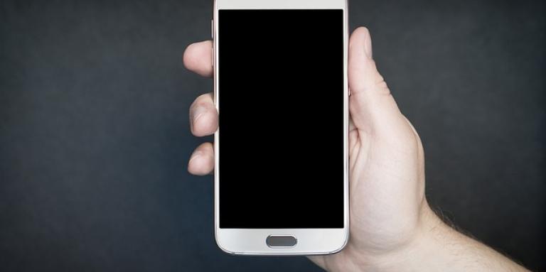 A hand holding an Android smartphone against a black background. 