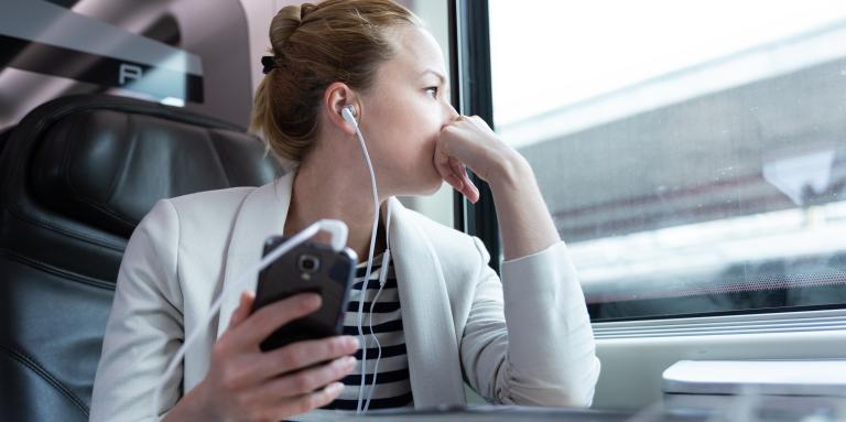 A woman has earbuds in and listens to a podcast on her smartphone. 