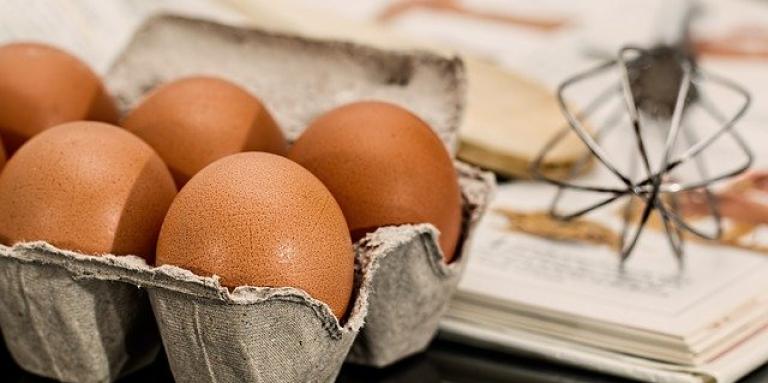 A carton of eggs. A whisk sits on a recipe book