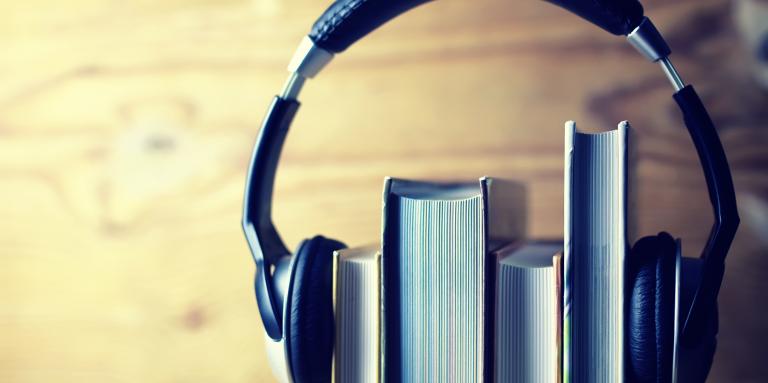 A stack of four books sits on a shelf. A pair of headphones sits on top of the books - holding them together. 