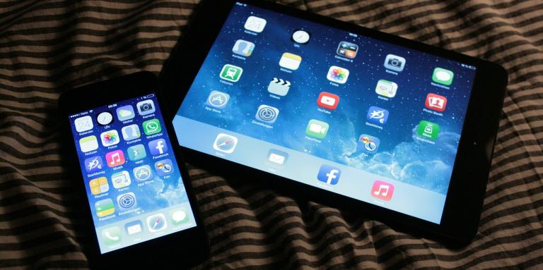 An iPhone and iPad sit side-by-side on a table top. 