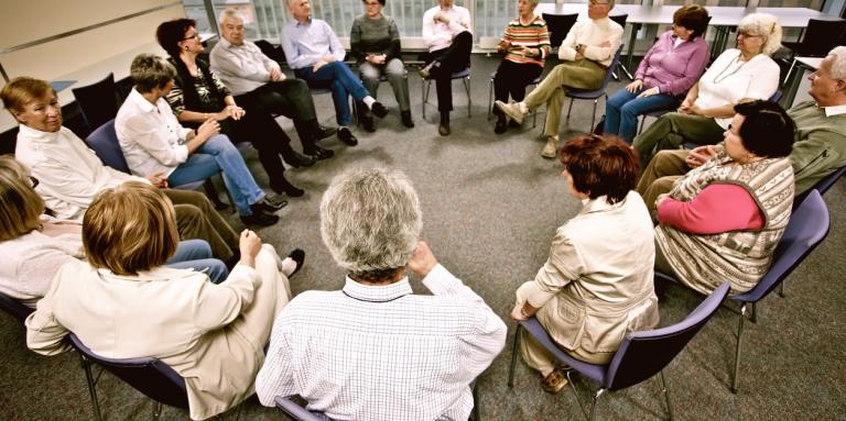 A group of 10 people sit in a circle and engage in lively conversation. 