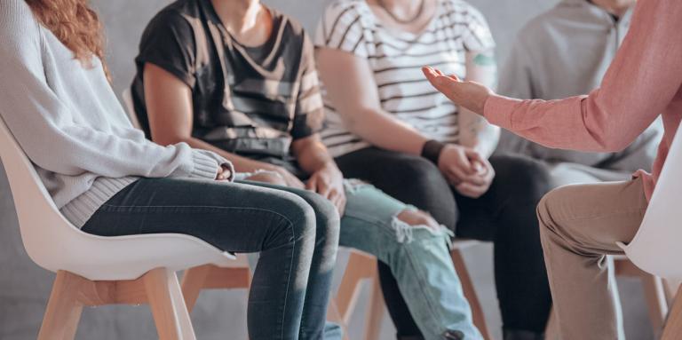 A group of five people sit in a circle and engage in lively conversation. 