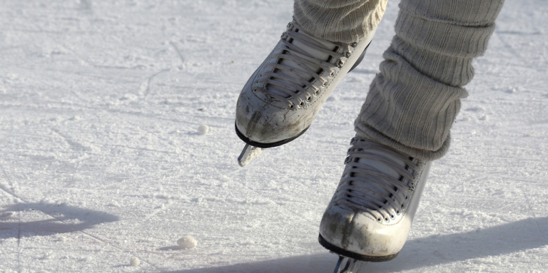 A pair of figure skates glide across an ice rink. 