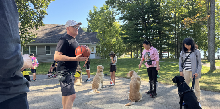 An instructor stands outside in front of a line of participants and guide dogs.