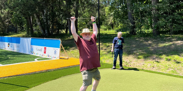 A man is standing in a mini putt course triumphantly holding a club over his head and smiling.