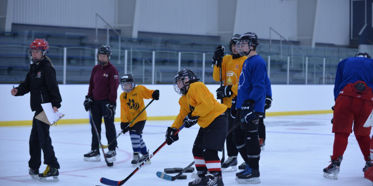 Coach guiding young players on the ice. Players are wearing yellow and blue jerseys