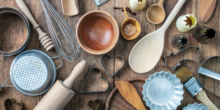 Bird's eye view of a variety of baking tools on a wooden table: spoons,, rolling pins, cookie cutters, etc.