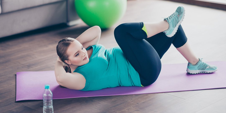 Woman exercising at home on a purple yoga mat. 