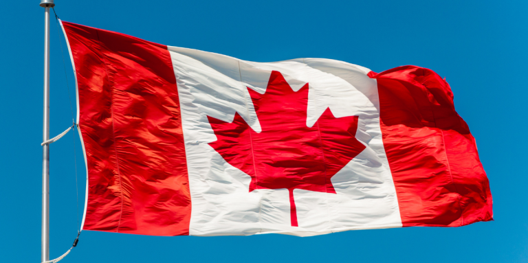 A Canadian flag waves on a flagpole against a bright blue sky.