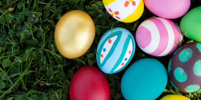 A pile of colourful dyed easter eggs sit atop a grassy lawn. 