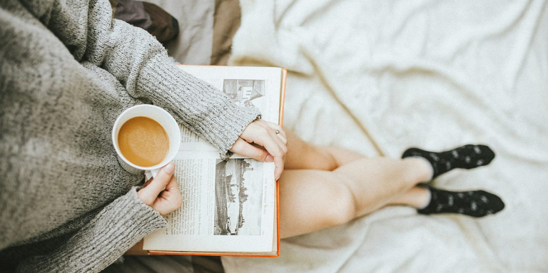 Birds eye view photo of a woman sitting with a coffee and a book on her lap.