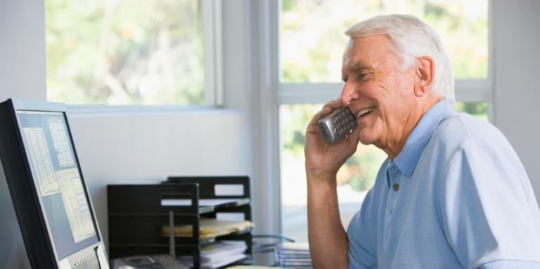 Elderly man talking on his phone in home office