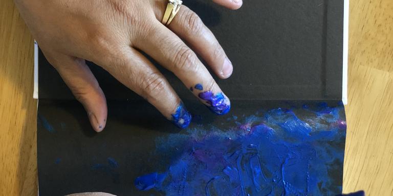 Close up of Neena's hands painting in blue on her sketch pad.