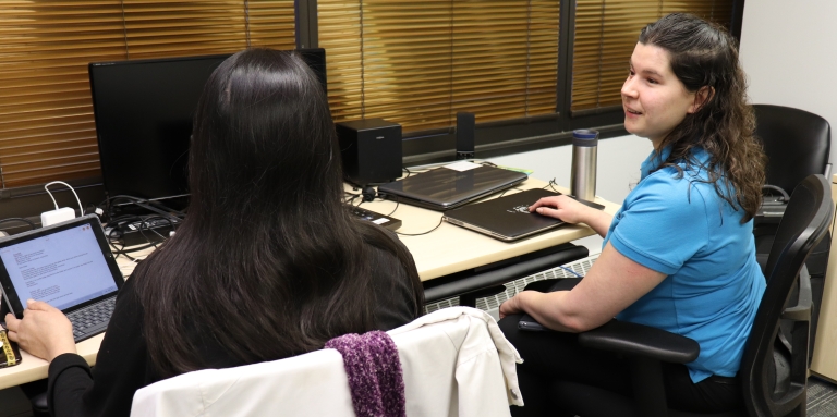 Charlene sits in front of of a computer helping a client learn technology