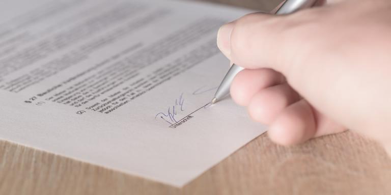 A woman's hand is shown signing a contract.