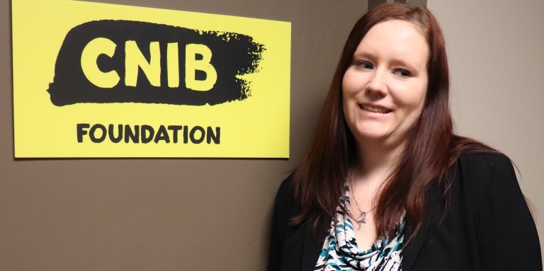 Paige Andreas smiles as she stands beside a CNIB Foundation sign