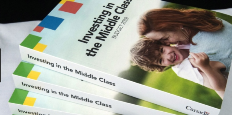 Copies of the 2019 budget booklet are stacked on a table. 