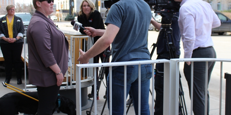 Ashley Nemeth and her guide dog stand outside of a restaurant being interviewed by the media