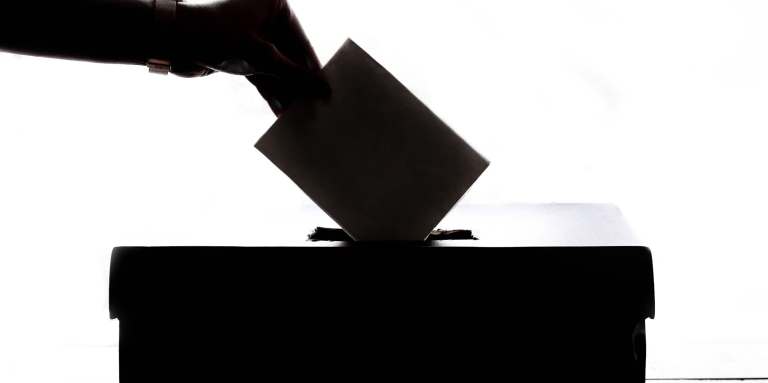 A shadow silhouette of a hand putting a vote into a box.  