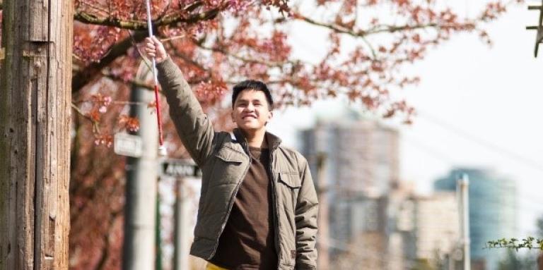A young man holds his white cane in the air triumphantly.  