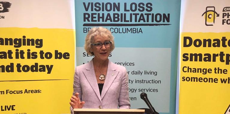 Minister Joyce Murray giving a speech in front of our CNIB and VLRC Banners