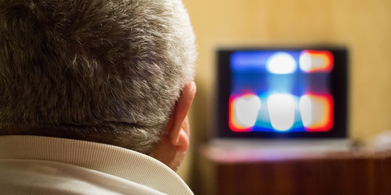 A man with grey hairs watching blury tv