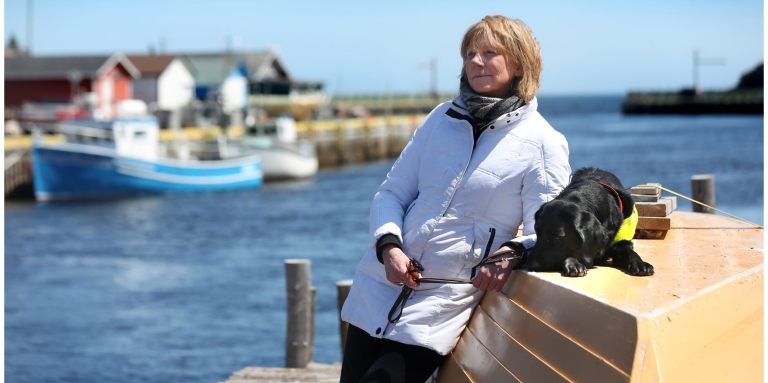 Anne Malone standing on the waterfront with her guide dog Cheryl