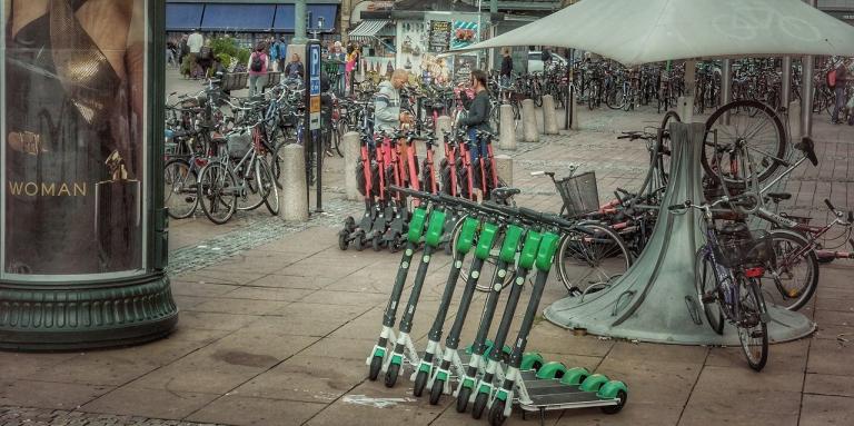  A city sidewalk with a row of electric scooters lined up on it.