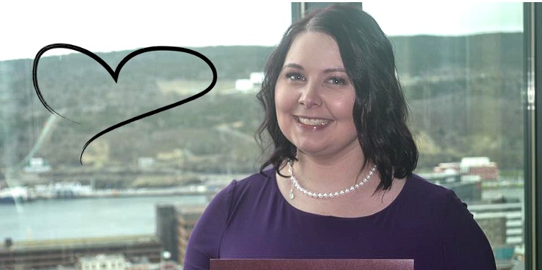 Brittany Farrell, smiling for the camera, standing in front of a window that overlooks the city of St. John’s, Newfoundland. A heart graphic can be seen against the window.