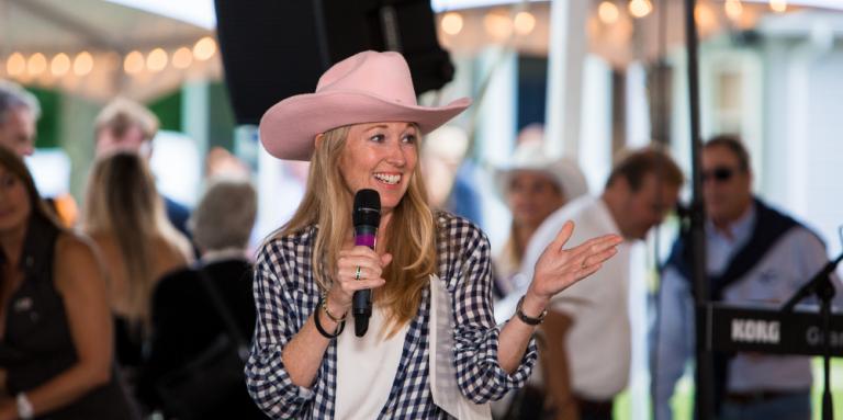 Nancy Simonot wearing a pink cowboy hat and speaking into a microphone at a Lake Joe fundraising event.