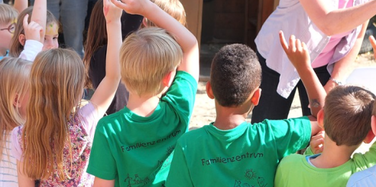 A group of young children raise their hands in the air to answer a question.