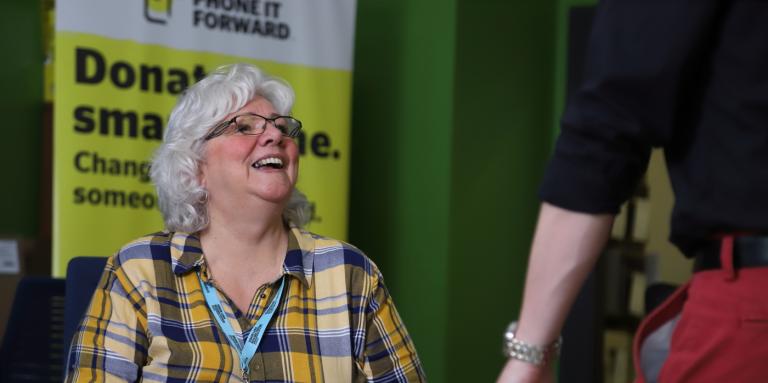 A smiling woman sitting behind a reception desk looks up at a visitor.