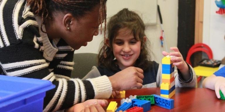 Sergeline aide une jeune fille souriante à construire un tour de lego.