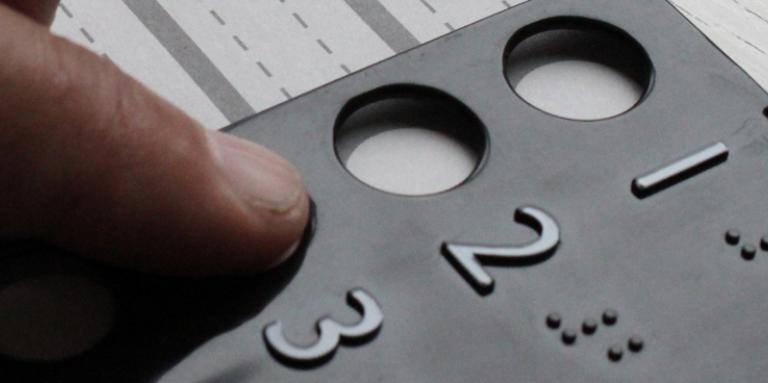 Close-up photo of a person's hands using a braille voting template.