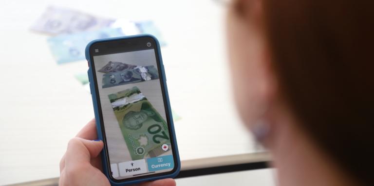 Money appears on the screen of an iPhone with the side of a woman's face in the foreground