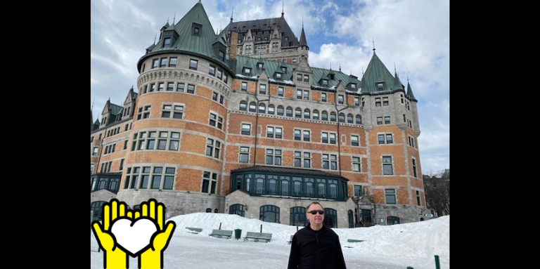 A picture of Louis Levesque standing in front The Château Frontenac. A yellow graphic of hands holding a white heart outlined in black in the bottom left corner.