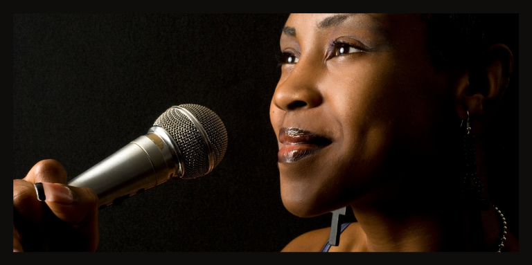 A young woman holds a microphone close to her mouth. She is smiling and preparing to sing.