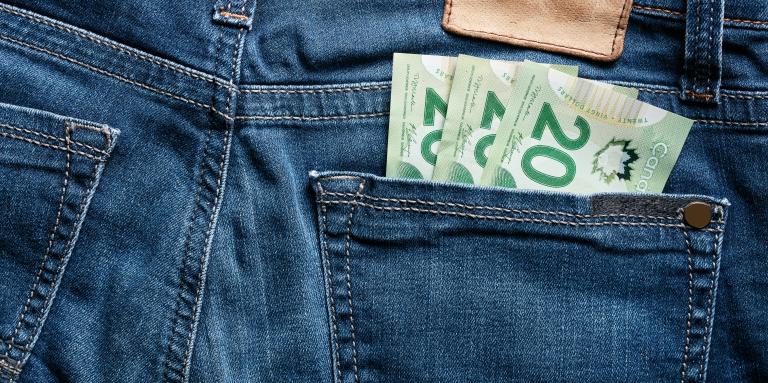 The backside of a pair of denim jeans. Three $20 bills are stuffed in the right hand pocket, 